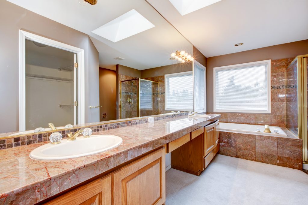Large lnew uxury bathroom with red granite countertops and tub.